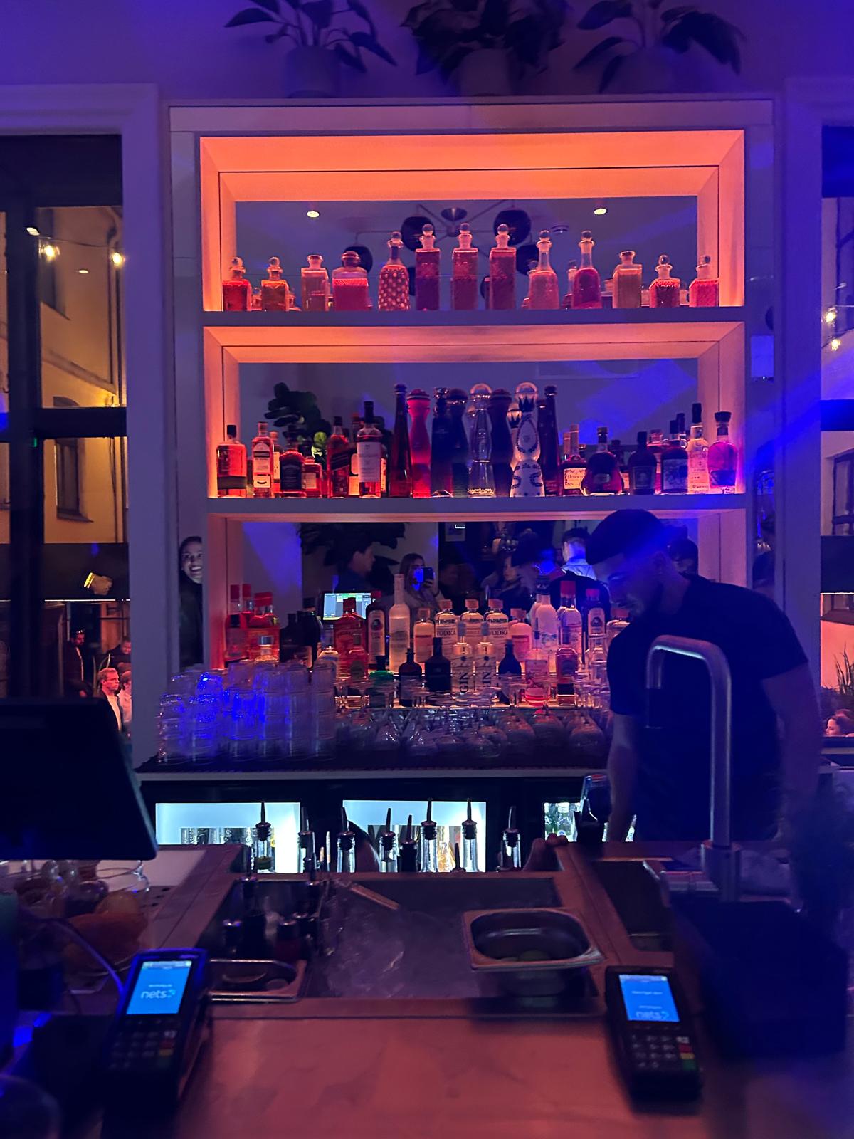 A bartender behind a colorful backlit bar